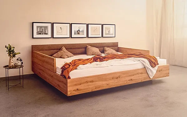 Rauminszenierung: Bett im Sonnenlicht. Beispiel für ansprechende Möbel- und Interieur-Fotografie für Ihr Portfolio. Modernes Holz- Familien- Doppelbett mit Stoffkopfteil und Dekoration im sonnendurchfluteten Schlafzimmer. Hochwertige Interieur- und Möbelfotografie.